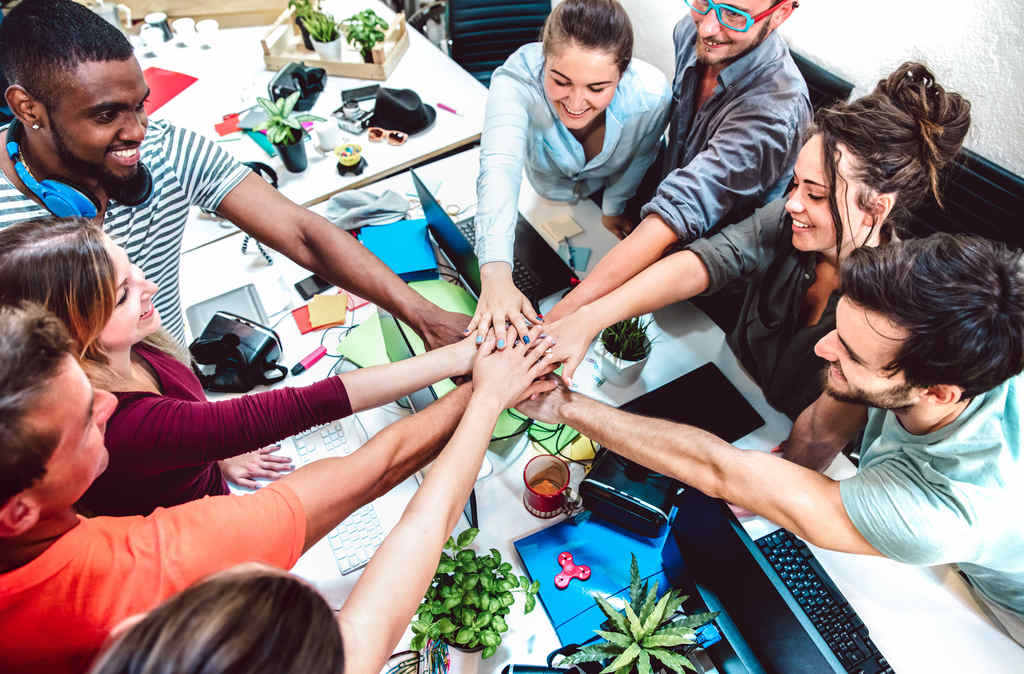 Grupo de pessoas sorrindo em ambiente de trabalho, unindo suas mãos no centro do grupo, simbolizando os processos de RH