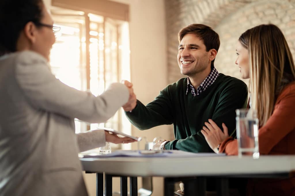 Homem sorrindo ao lado de sua esposa, cumprimentando uma advogada, simbolizando como receber indenização por acidente de trabalho